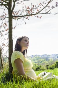 אישה בהריון יושבת ליד עץ